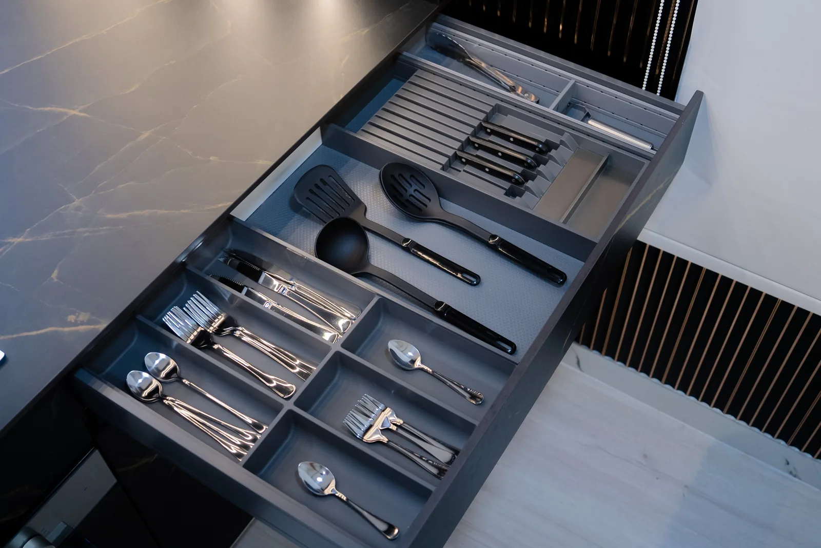 Open kitchen drawer beside a dark veined stone worktop, showing the drawer assembly.