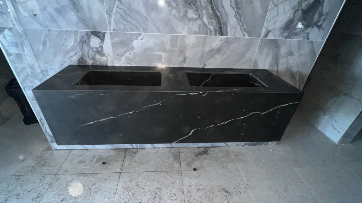 Double stone basin and floating vanity against veined wall.