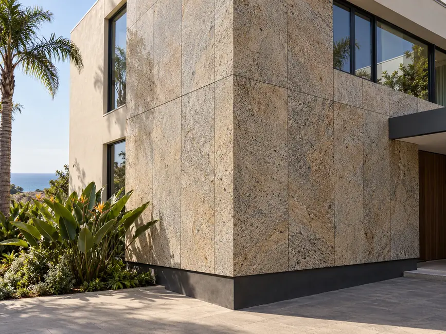 Vertical speckled granite panels meet a dark plinth beside glazing and subtropical planting.