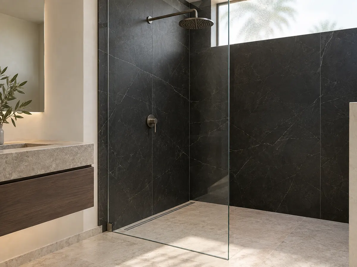 Black stone shower panels meet a pale drained floor behind a glazed screen with one mixer and shower head.