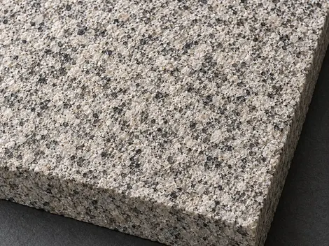 Flamed warm-grey granite sample with a coarse matt face, angular mineral grains and a solid exposed edge.