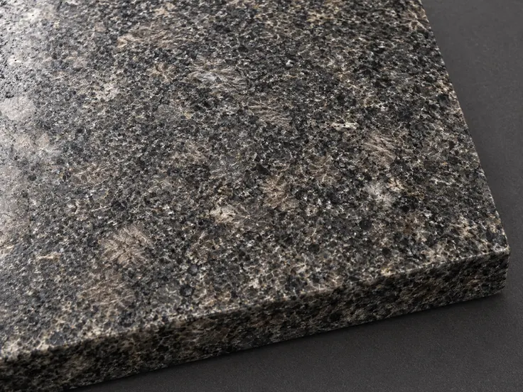 Charcoal-grey granite sample with interlocking pale and dark mineral grains and a solid exposed edge.