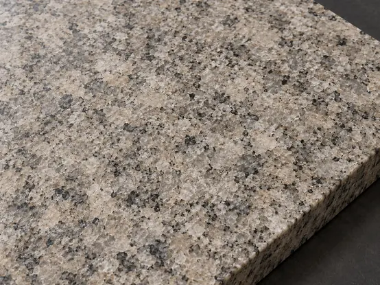 Honed warm-grey granite sample with a smooth matt face and pale and dark mineral grains.