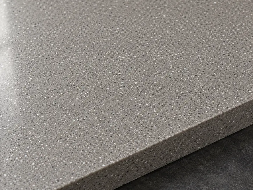 Warm grey quartz sample with fine pale and dark aggregate and a smooth exposed edge.
