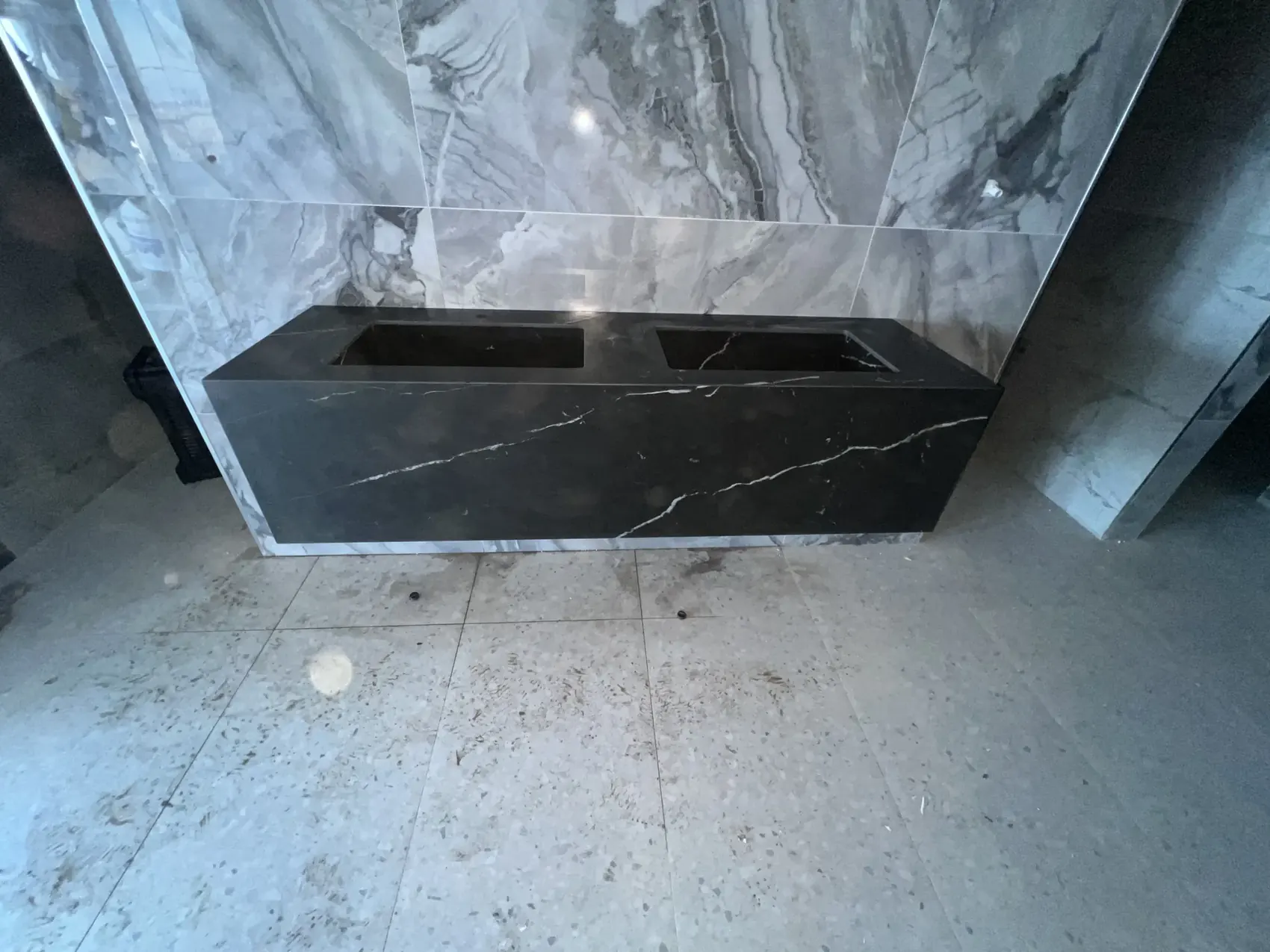 Dark wall-mounted vanity with two basin openings against a veined wall.